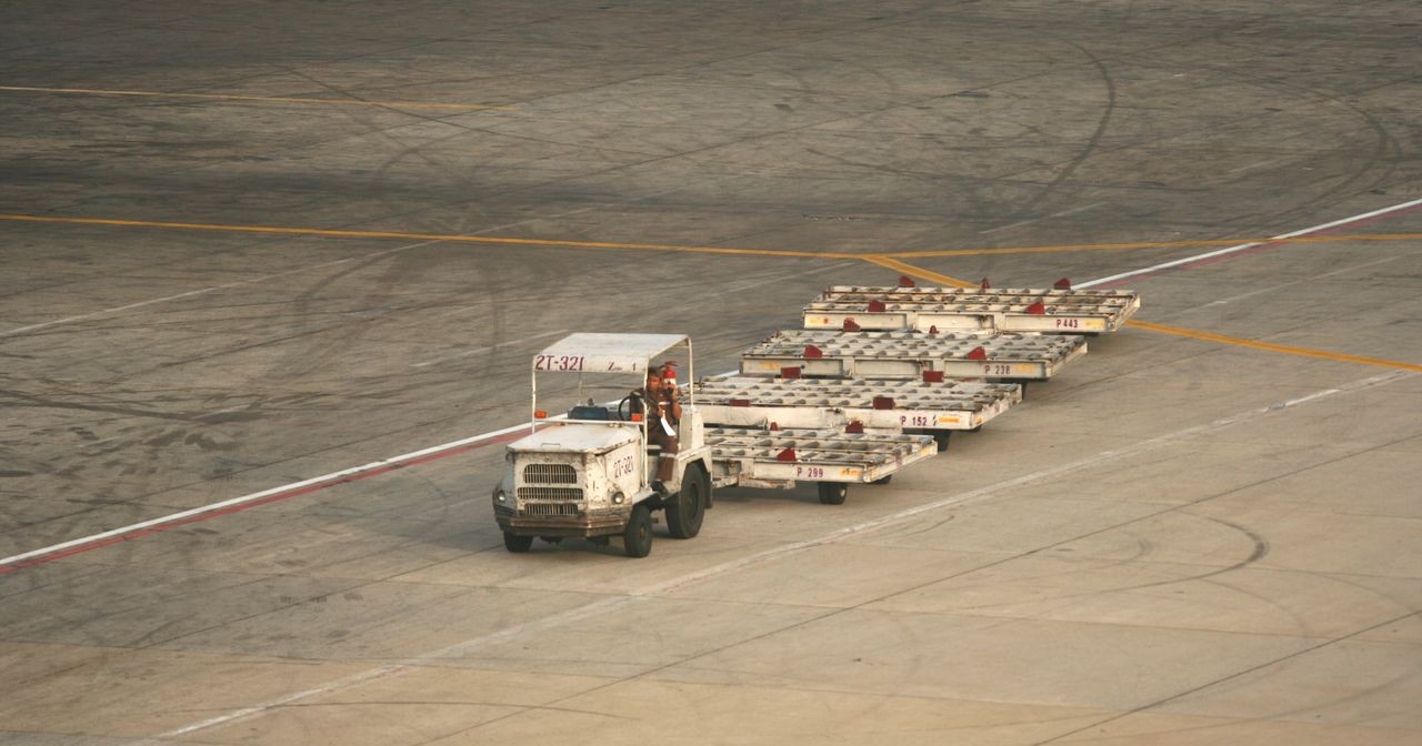 A tug pulling a train of empty baggage carts across the apron