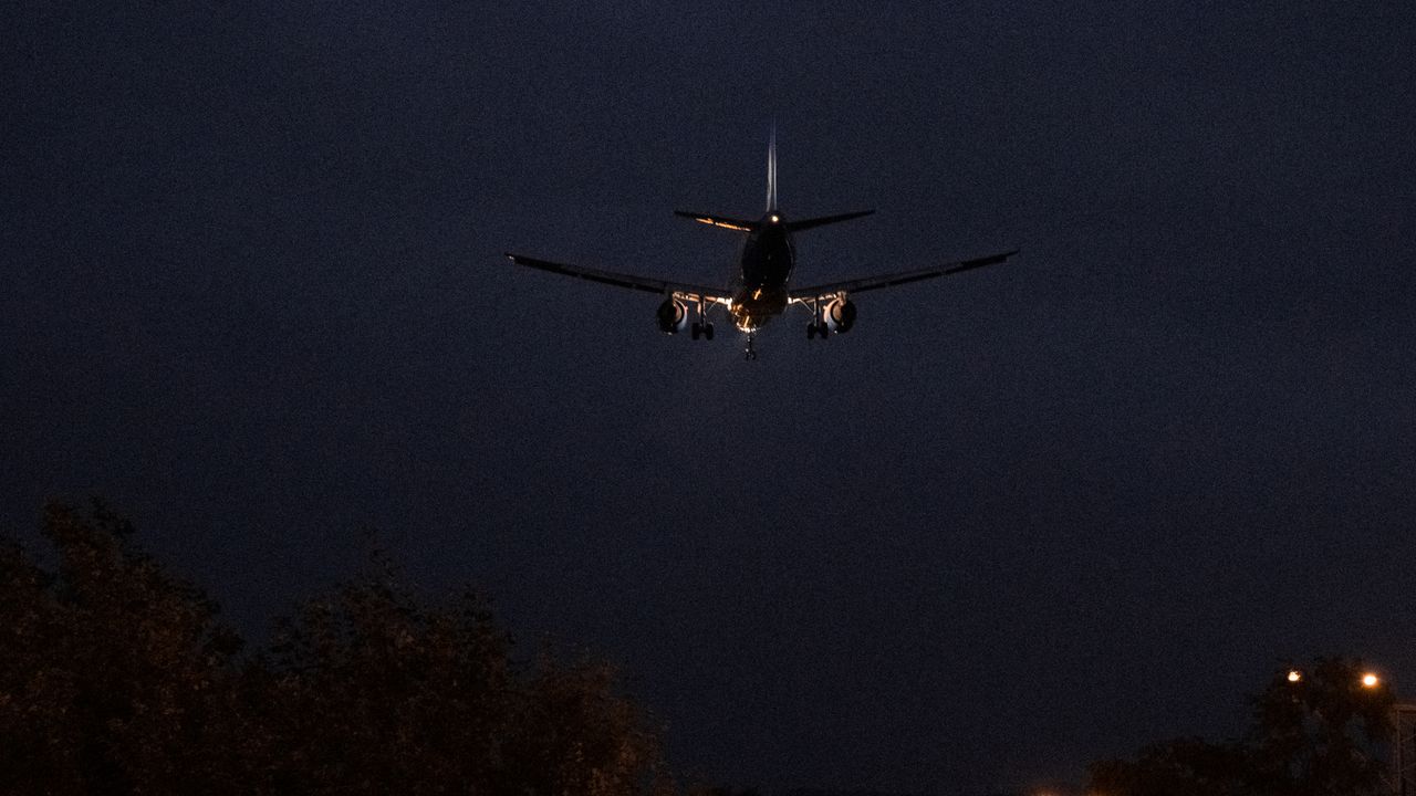 An aircraft on final approach at night, landing lights lit against a dark sky